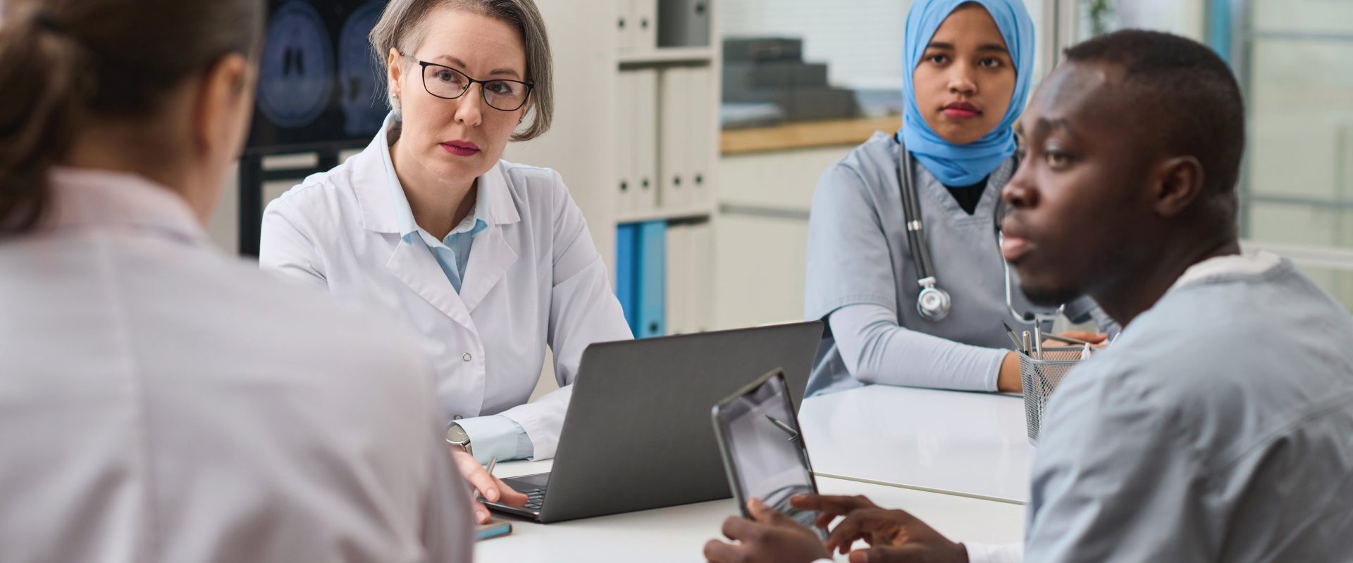 Group of doctors listening to their colleague while using gadgets during teamwork at meeting